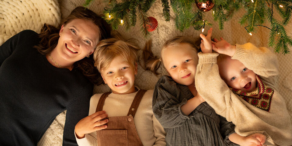 Familie liegt entspannt auf dem Boden unter einem Weihnachtsbaum mit Lichtern.